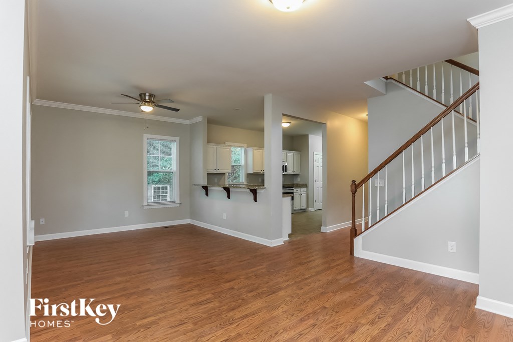 A spacious room with wooden floors and a staircase on the right side.