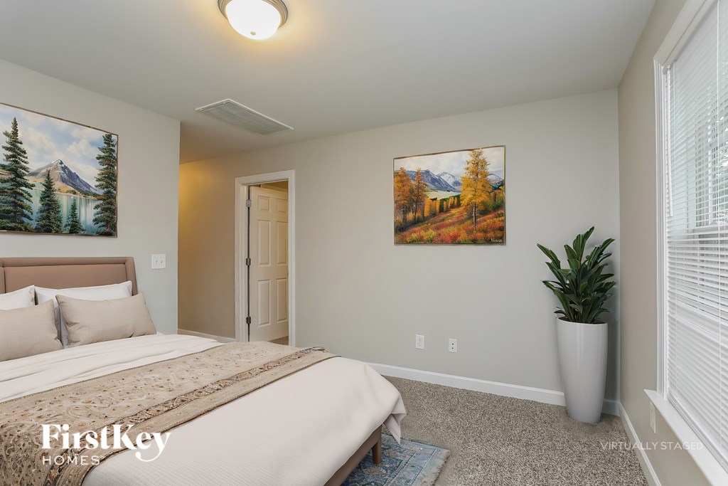 A bedroom with a bed, a painting, and a plant.