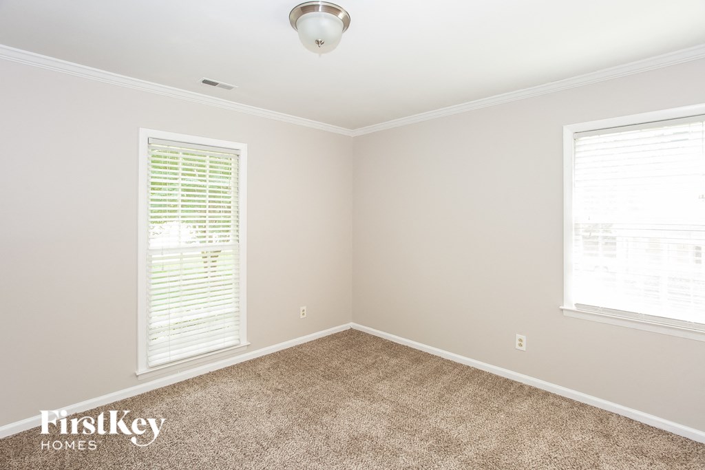 A room with a carpeted floor, a window with blinds, and a ceiling light.