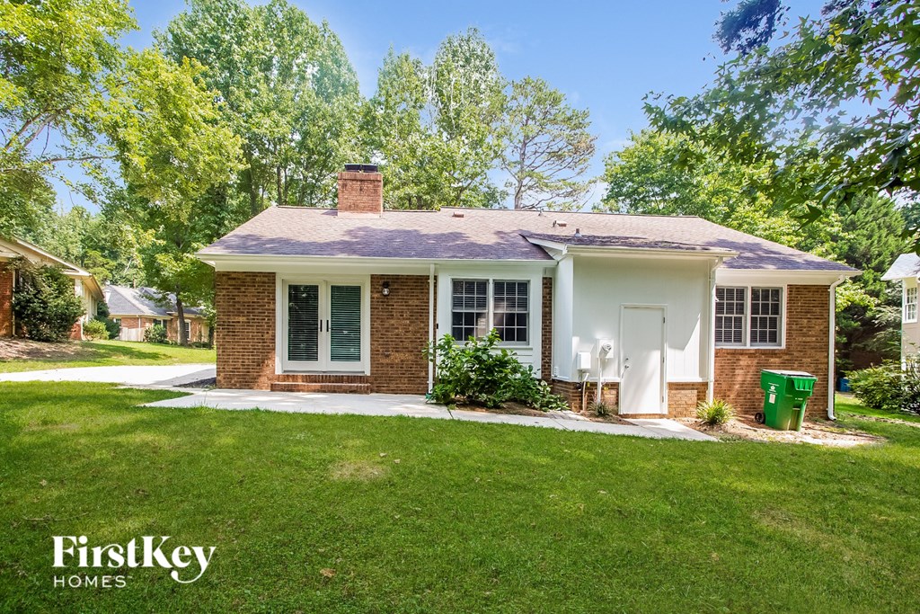 A brick house with a white door and windows is surrounded by green grass and trees.