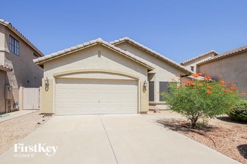 A beige house with a garage door and a small tree with orange flowers in front.