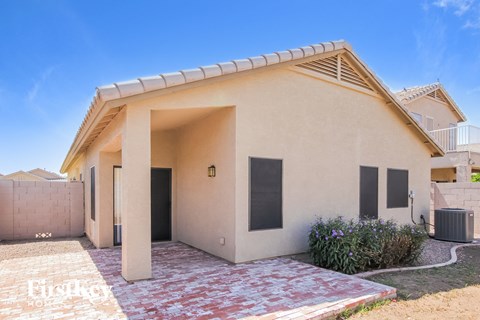 A small beige house with a red brick walkway in front.
