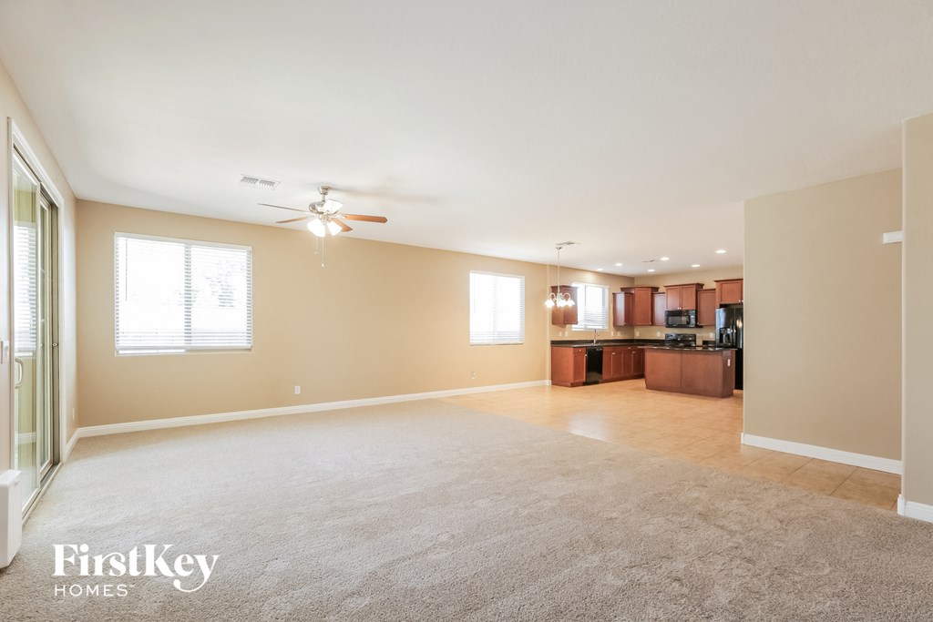 an empty living room with a ceiling fan and a kitchen