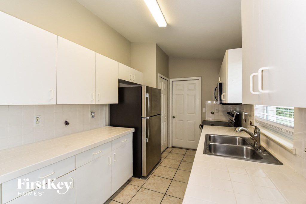 A kitchen with white cabinets and a black refrigerator.