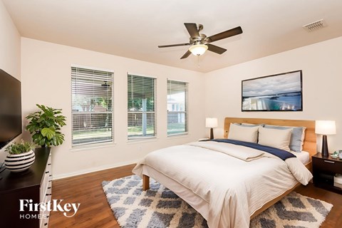 A bedroom with a bed, a ceiling fan, and a painting on the wall.