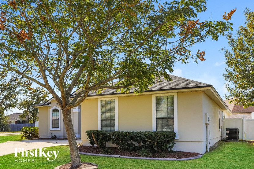 A tree with orange leaves stands in front of a house with the sign "FirstKey Homes" on the front lawn.