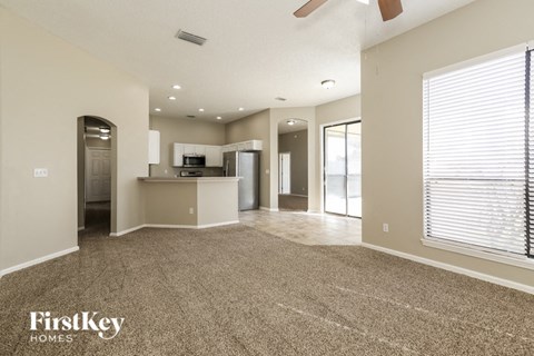 A spacious living room with a kitchen in the background and a carpet on the floor.