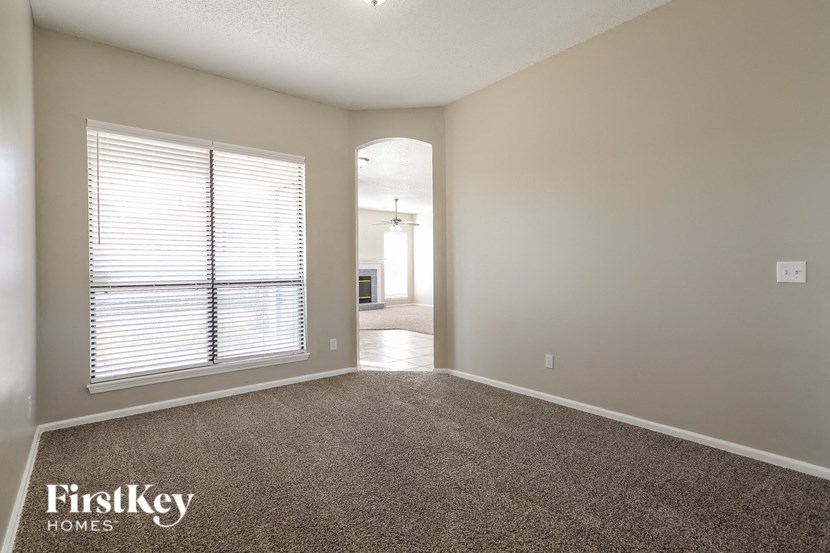 A spacious room with a carpeted floor and a window with blinds.