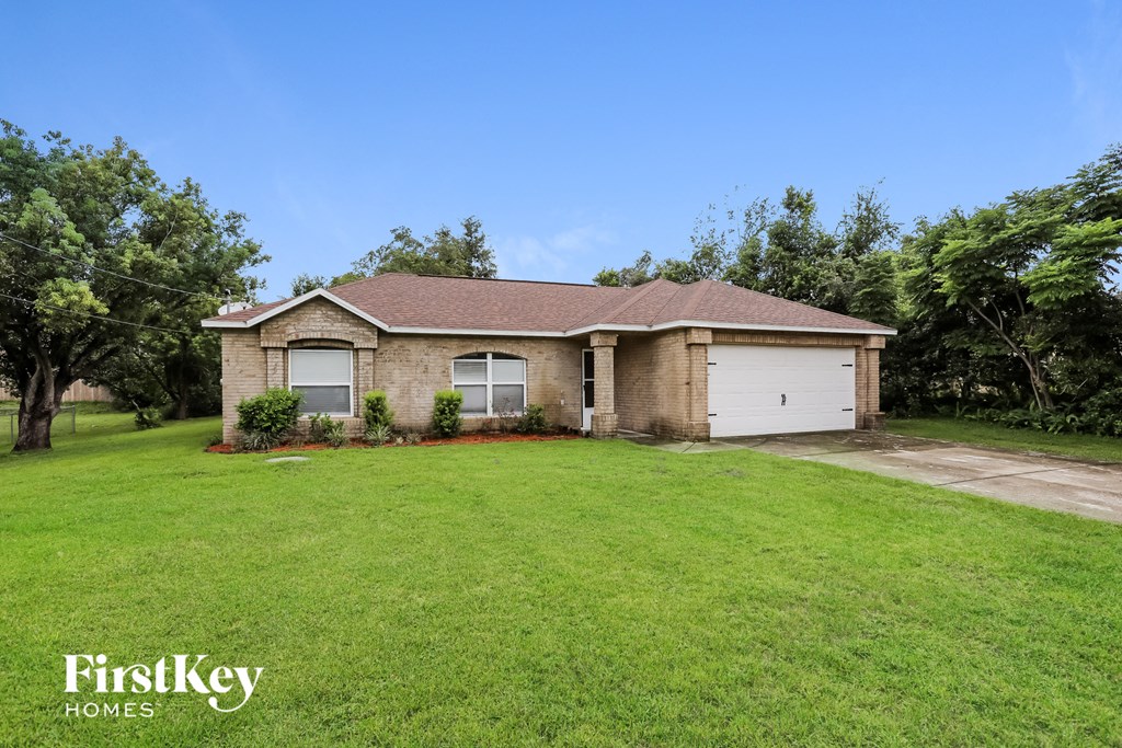A house with a brown roof and a white garage door is surrounded by a green lawn.