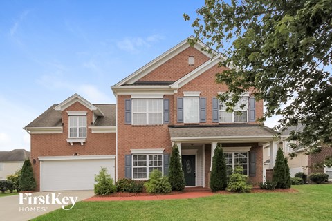 A brick house with a white garage door and a tree in front.