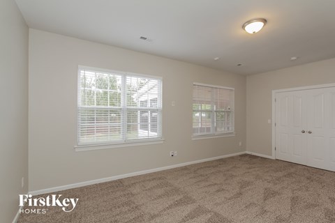 A room with a carpet floor, two windows with blinds, and a white door.