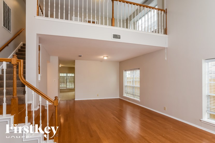 A spacious living room with wooden floors and a staircase leading to the upper level.