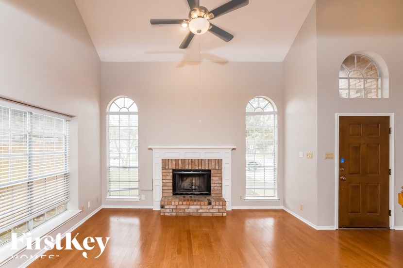 A large, empty room with a fireplace and a ceiling fan.