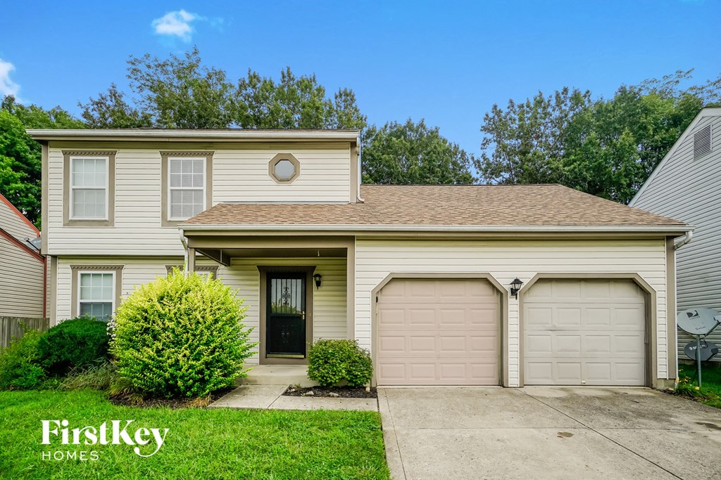 a beige house with two garage doors and a driveway