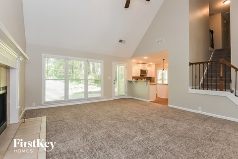A spacious living room with a staircase on the right and a kitchen area in the background.