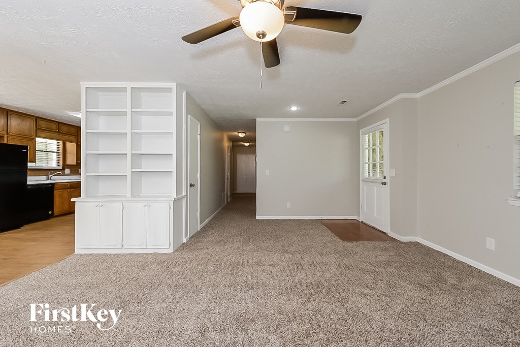 an empty living room with a ceiling fan and white shelves