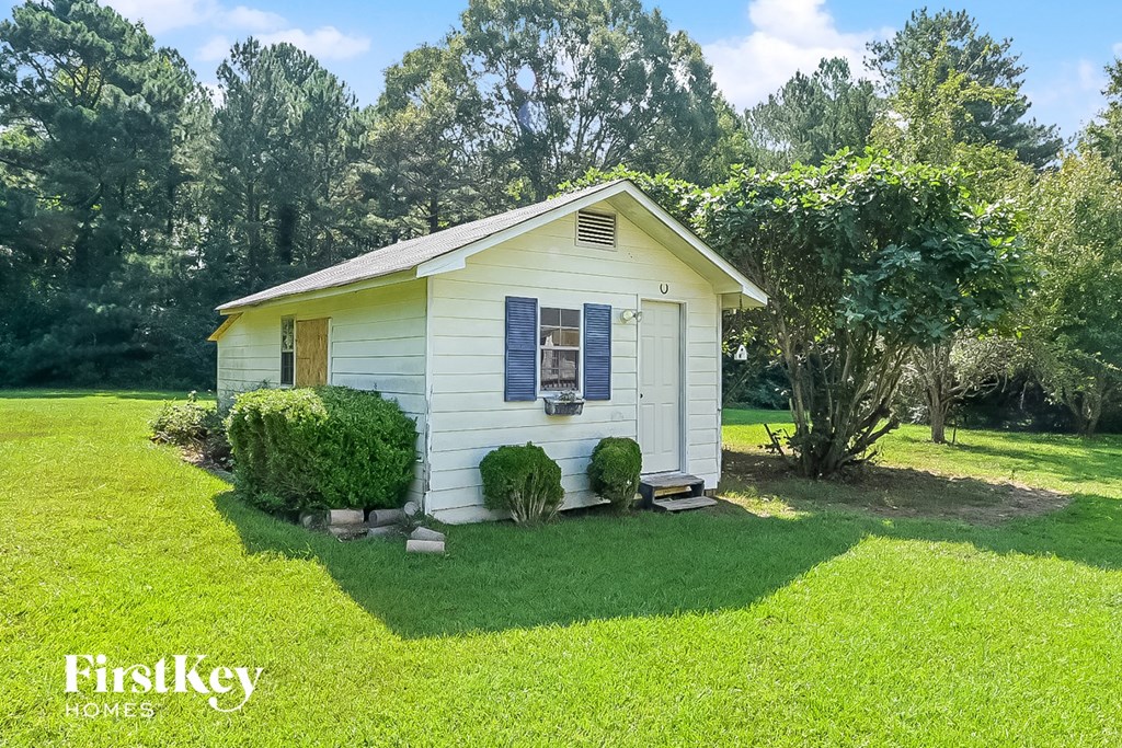 a small white house with blue shutters and a lawn and trees