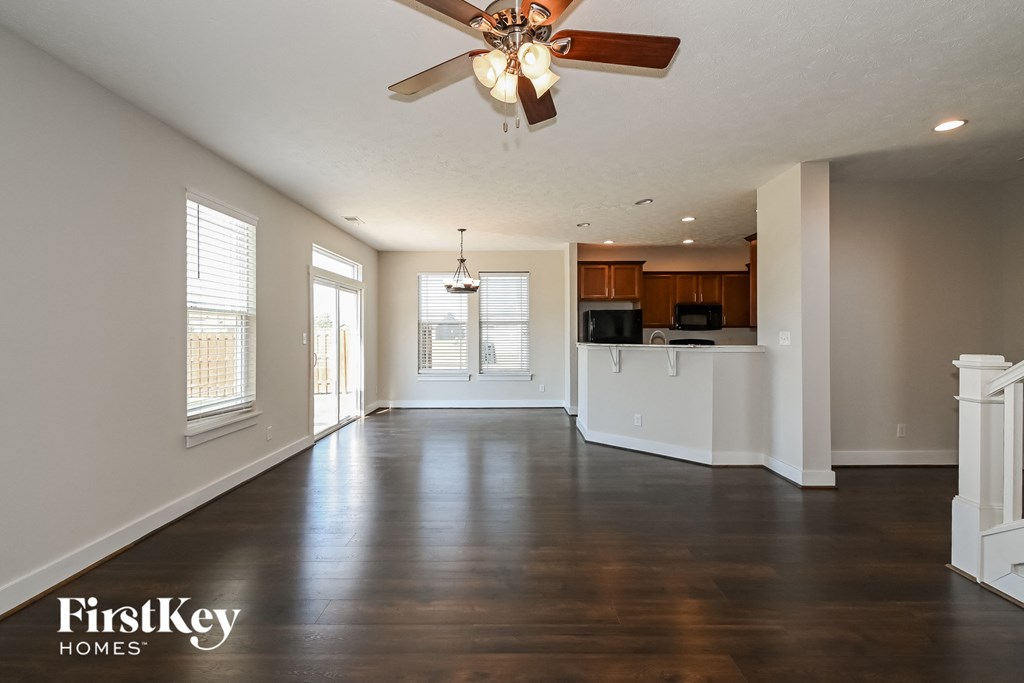 an empty living room with a ceiling fan and a kitchen