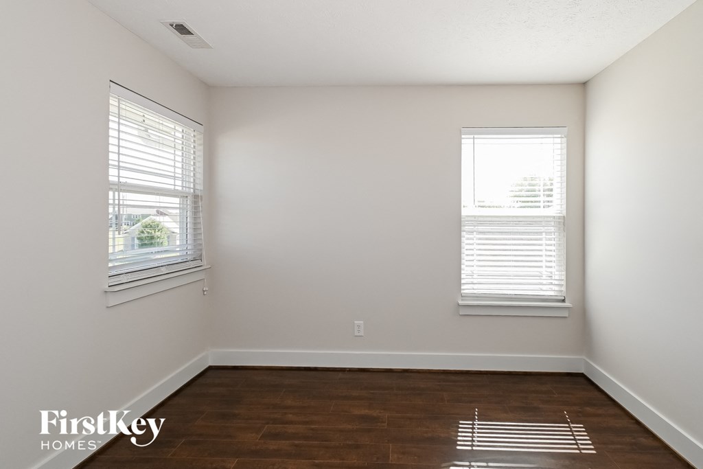 a bedroom with wood floors and white walls and two windows