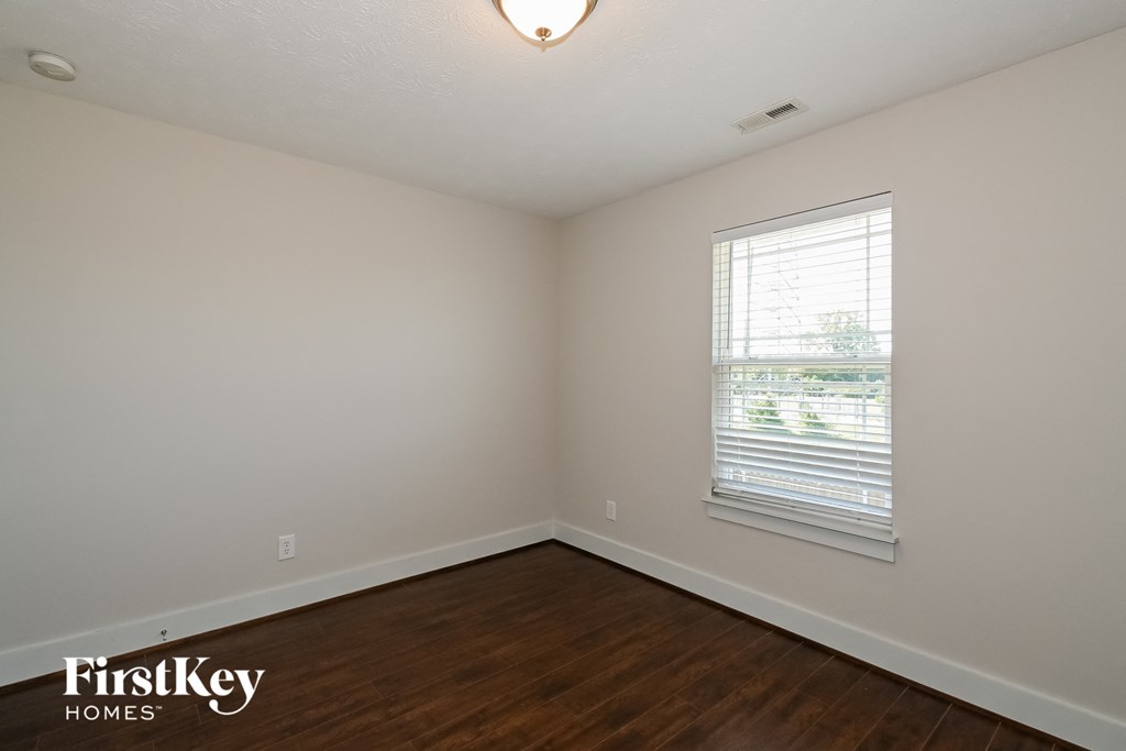 a bedroom with white walls and wood floors and a window