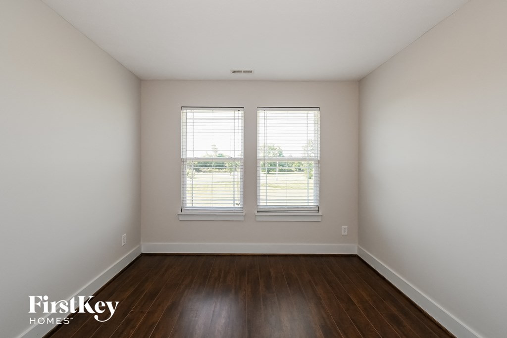 a bedroom with white walls and wood floors and two windows