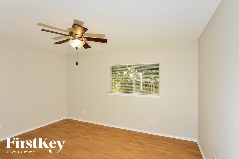 A room with a ceiling fan and a window with a view of a fence and trees.