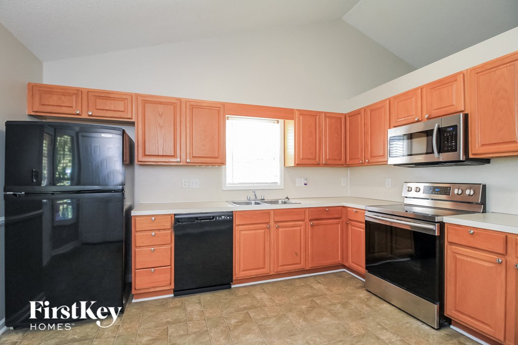A kitchen with orange cabinets and a black refrigerator.