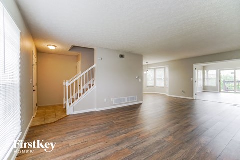 A spacious room with wooden floors and a staircase leading to another room.