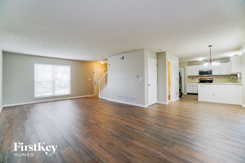 A spacious living room with wooden floors and a kitchen area in the background.