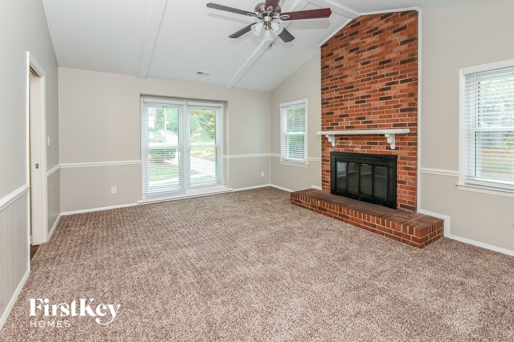 an empty living room with a brick fireplace and a ceiling fan
