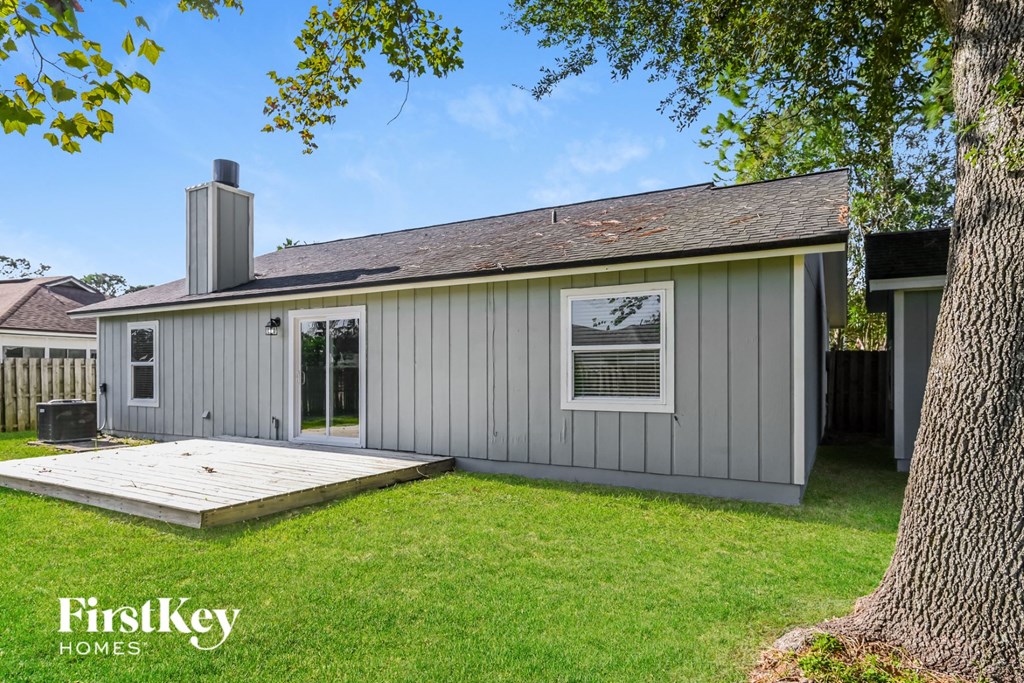 the backyard of a gray house with a deck and a tree