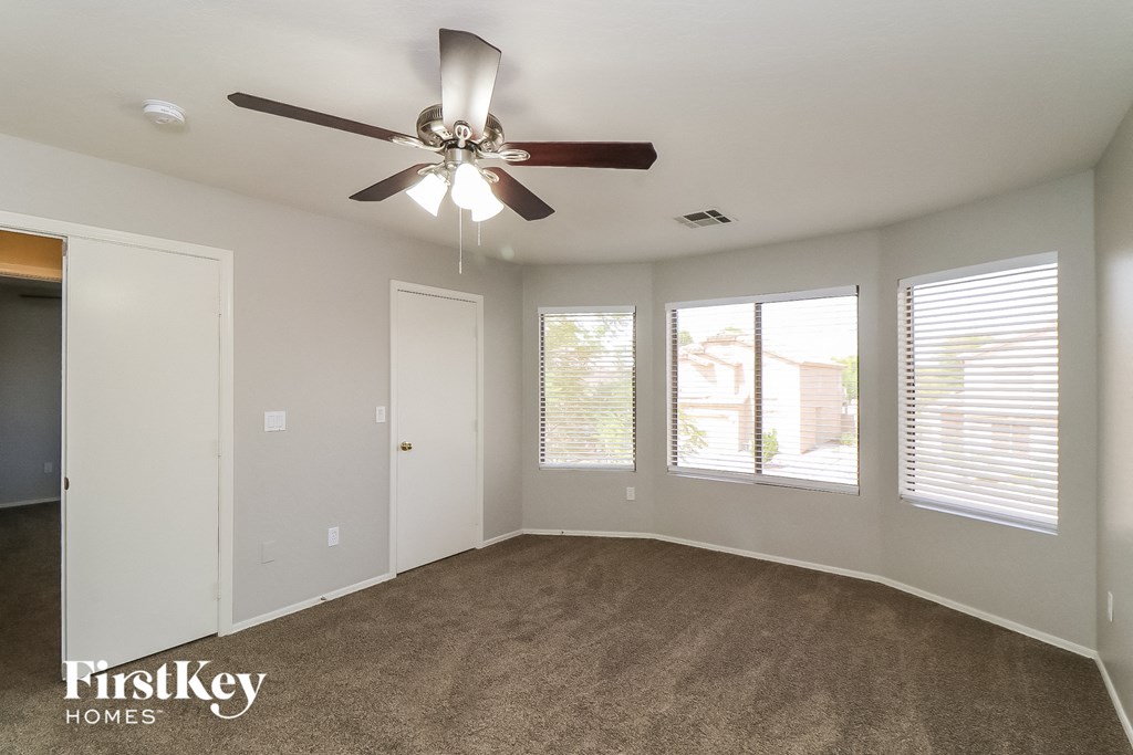 an empty living room with a ceiling fan and three windows