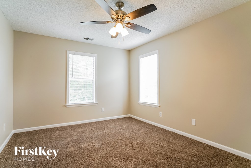 a carpeted living room with a ceiling fan and two windows