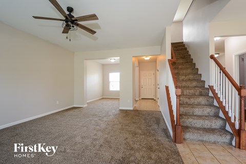 a carpeted living room with stairs and a ceiling fan