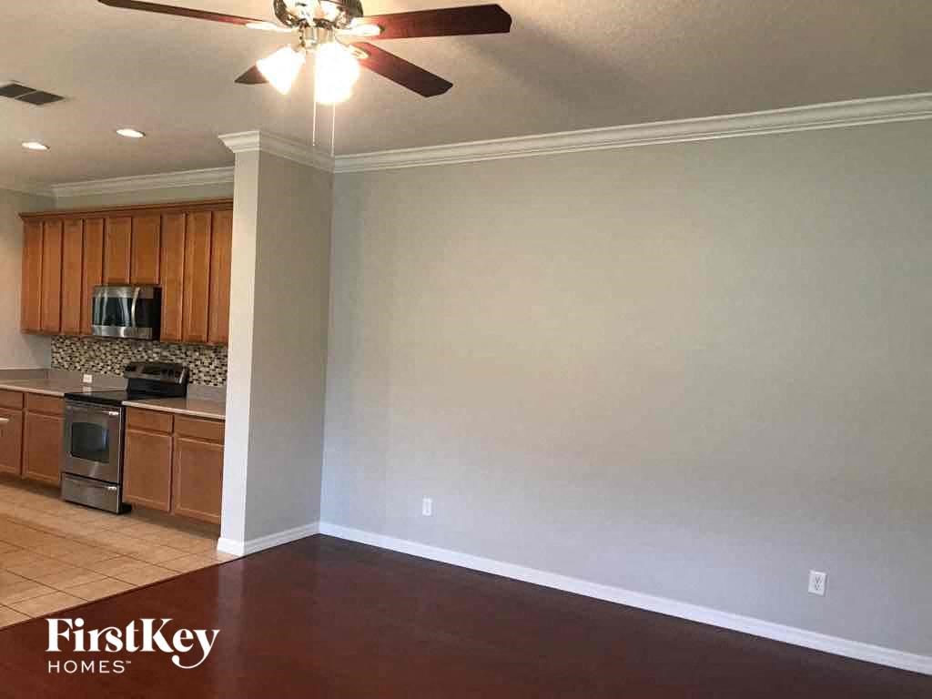 A room with a ceiling fan and a kitchen area in the background.