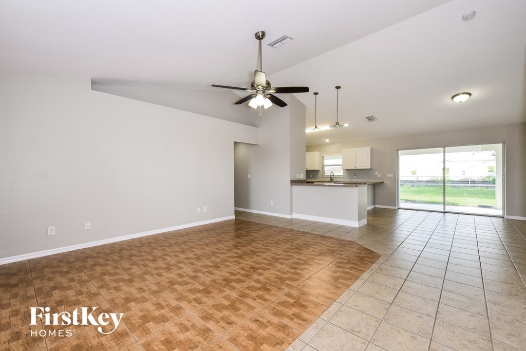an empty living room with a ceiling fan and a kitchen