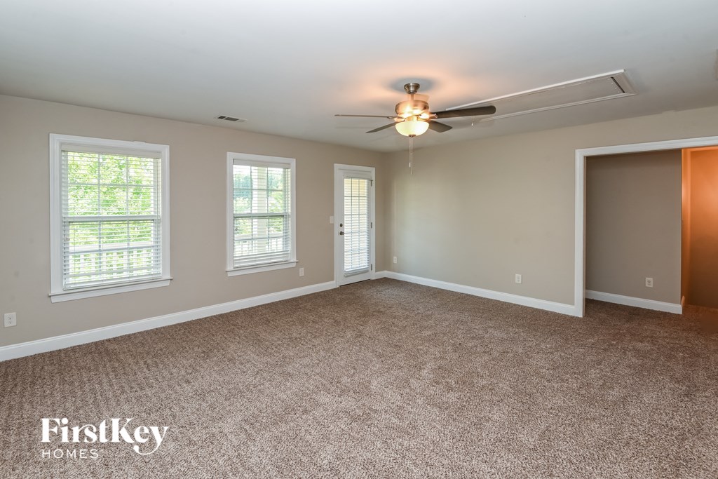 an empty living room with a ceiling fan and three windows