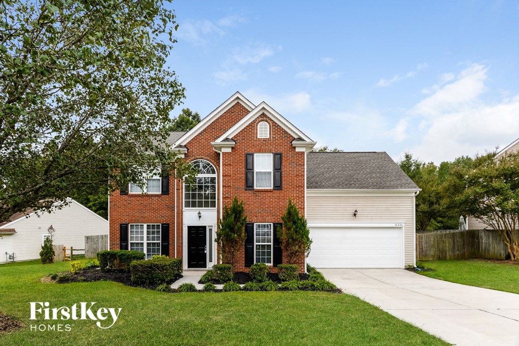 A brick house with a garage and a tree in front.