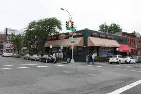 A street corner with a pizza shop and cars parked on the side of the road.