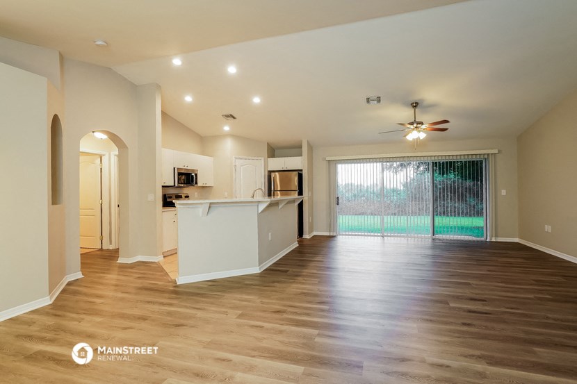 an empty living room with a kitchen and a sliding glass door