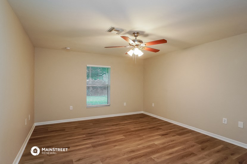 the spacious living room with hardwood flooring and a ceiling fan