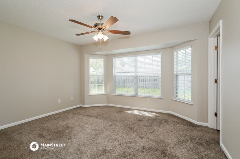 the spacious living room with large windows and a ceiling fan