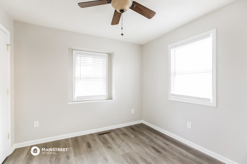 an empty room with a ceiling fan and two windows