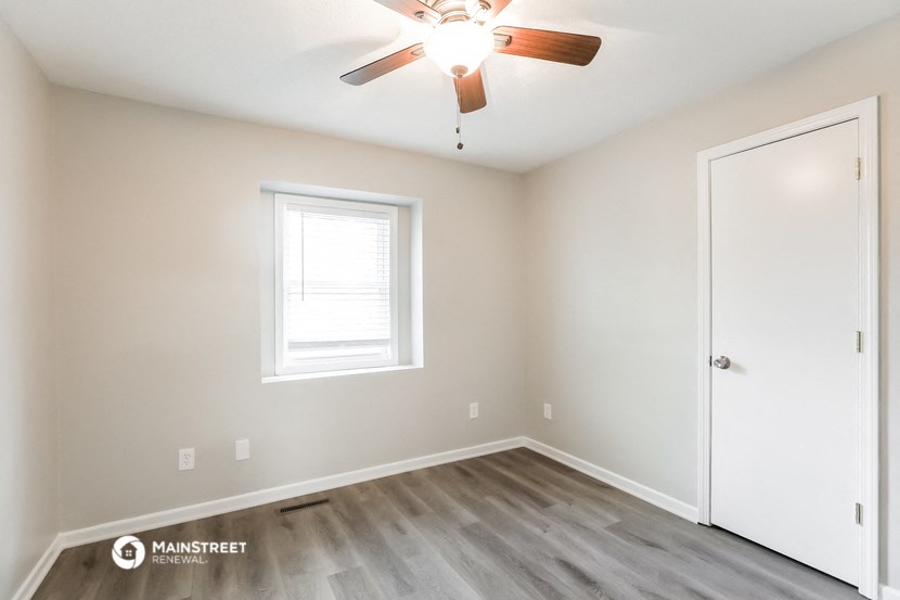 the spacious bedroom with hardwood flooring and a ceiling fan