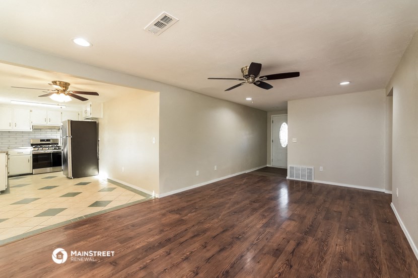 an empty living room and kitchen with wood flooring and ceiling fans
