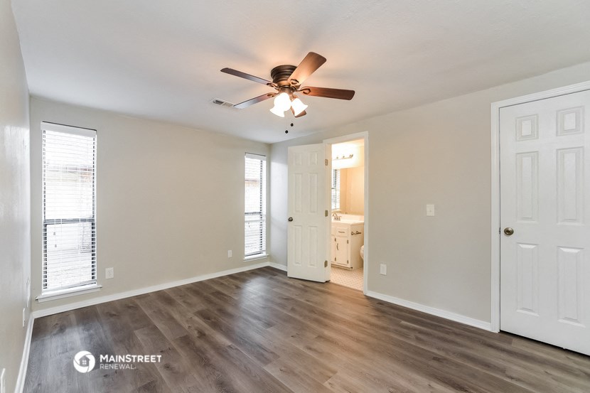an empty living room with a ceiling fan and a door to a bathroom