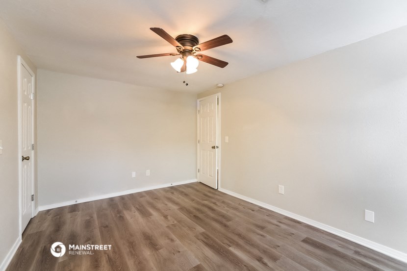 the spacious living room with wood flooring and ceiling fan