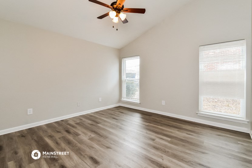 the spacious living room with a ceiling fan and two windows