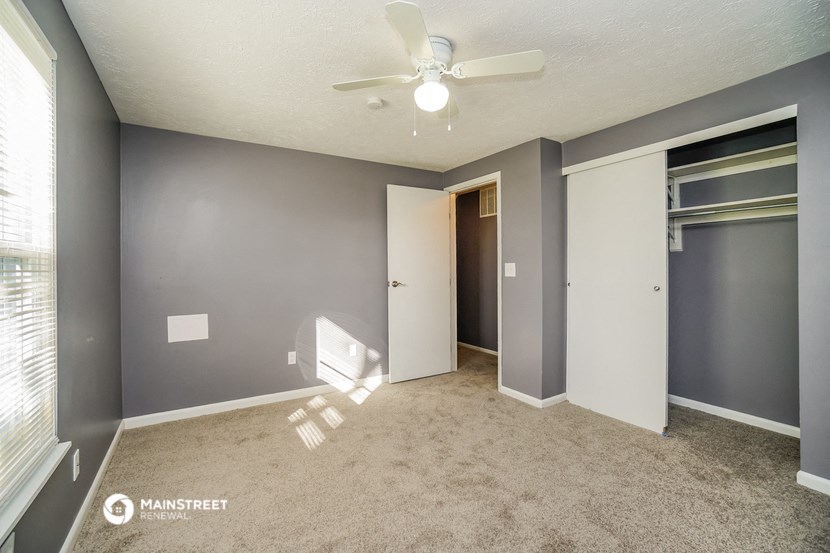 an empty living room with a ceiling fan and a closet