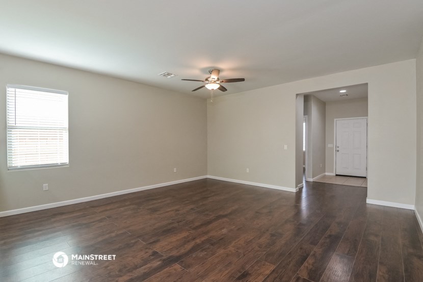 the spacious living room with wood flooring and a ceiling fan